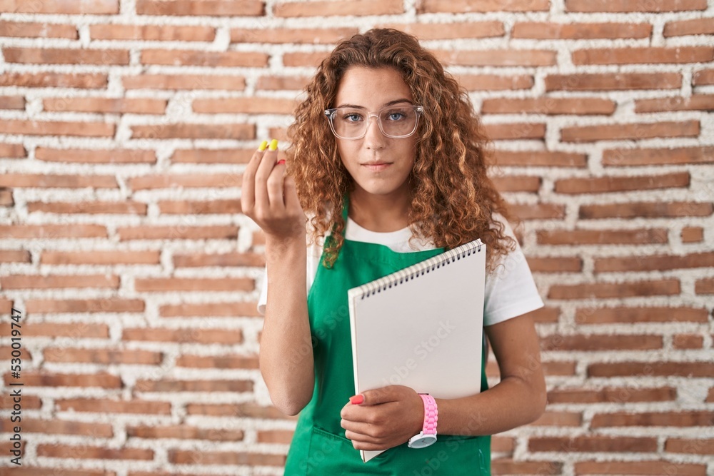 Young caucasian woman holding art notebook doing italian gesture with hand and fingers confident expression