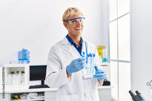 Young caucasian man wearing scientist uniform holding test tube at laboratory