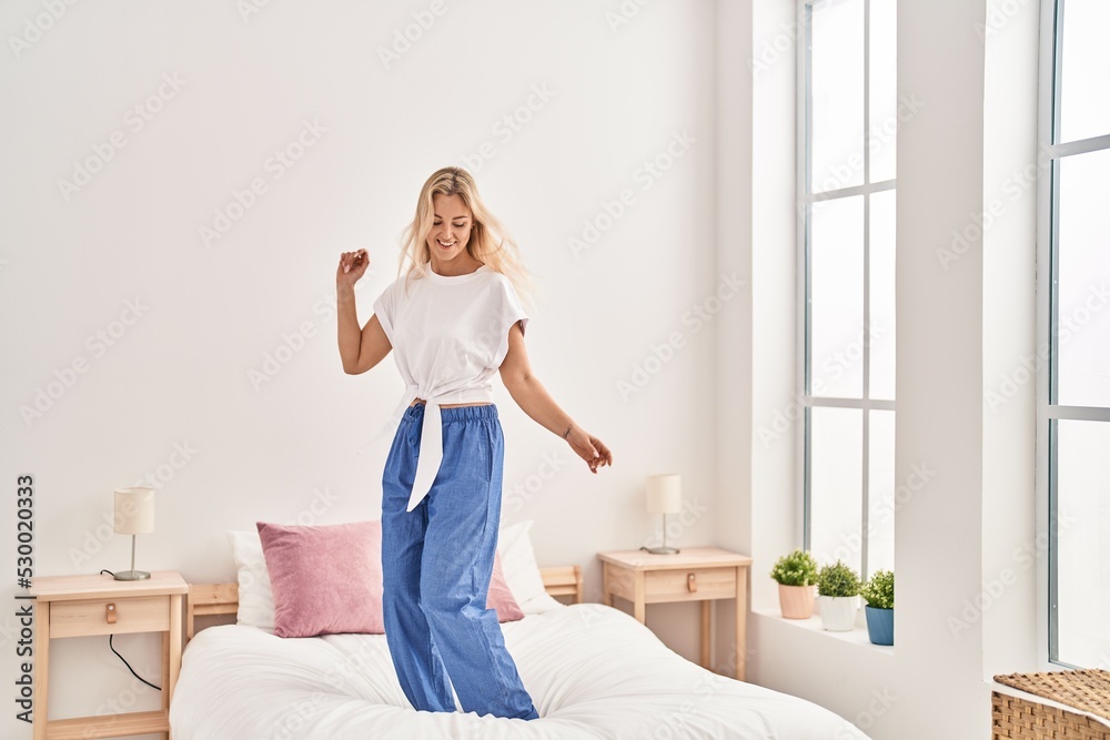 Young blonde woman dancing on bed at bedroom