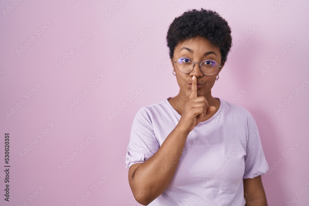 Young african american woman standing over pink background asking to be quiet with finger on lips. silence and secret concept. Young african american woman standing over pink background asking to be quiet with finger on lips. silence and secret concept.