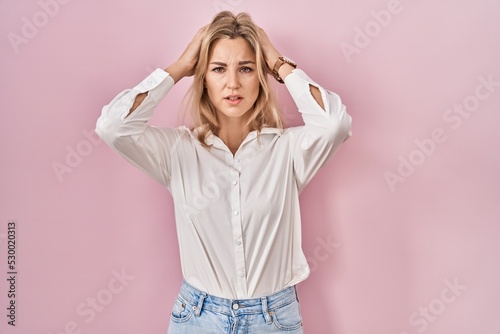 Young caucasian woman wearing casual white shirt over pink background suffering from headache desperate and stressed because pain and migraine. hands on head. © Krakenimages.com