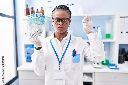 African woman with braids working at scientist laboratory holding money skeptic and nervous, frowning upset because of problem. negative person.