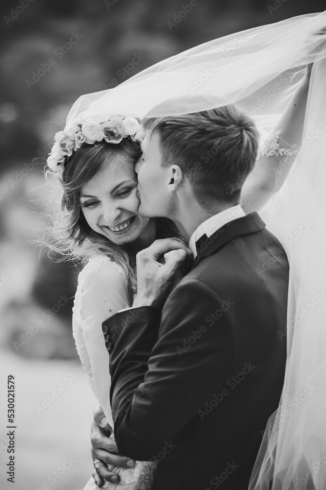Romantic wedding moment, bride and groom smiles to each other under the veil, happy and joyful moment on nature in the park. Black and white photo.