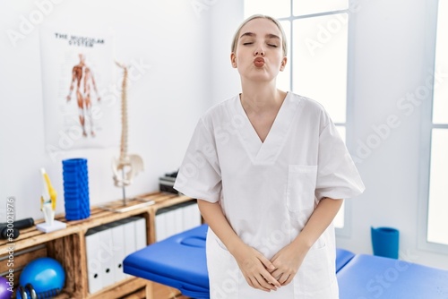 Young caucasian woman working at pain recovery clinic looking at the camera blowing a kiss on air being lovely and sexy. love expression.