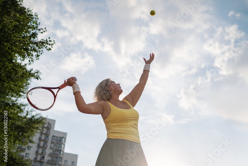 mature woman playing tennis serving a ball outside.