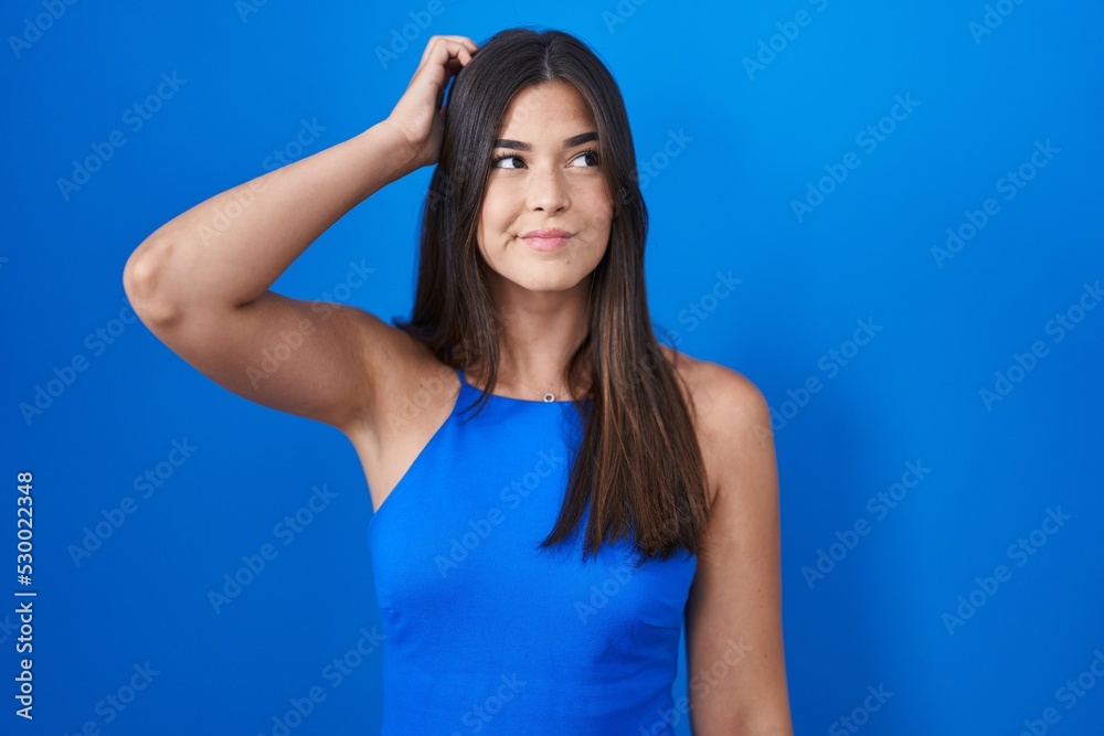 Hispanic woman standing over blue background confuse and wondering about question. uncertain with doubt, thinking with hand on head. pensive concept. Hispanic woman standing over blue background confuse and wondering about question. uncertain with doubt, thinking with hand on head. pensive concept.