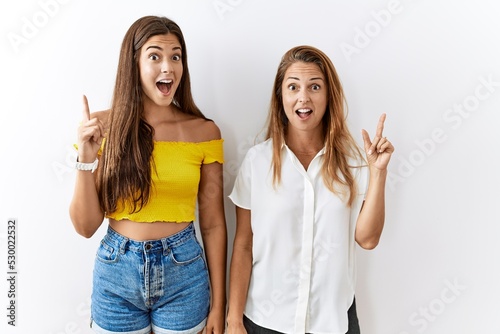 Mother and daughter together standing together over isolated background pointing finger up with successful idea. exited and happy. number one.