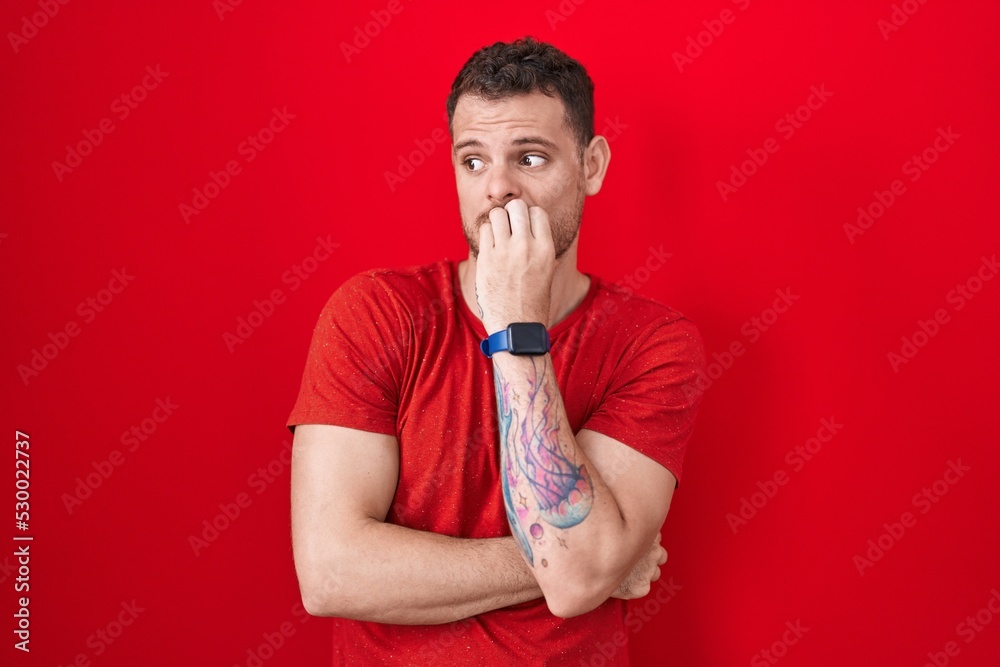 Young hispanic man standing over red background looking stressed and nervous with hands on mouth biting nails. anxiety problem. Young hispanic man standing over red background looking stressed and nervous with hands on mouth biting nails. anxiety problem.