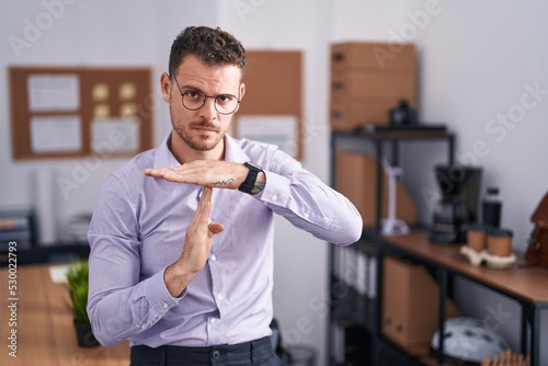 Young hispanic man at the office doing time out gesture with hands, frustrated and serious face