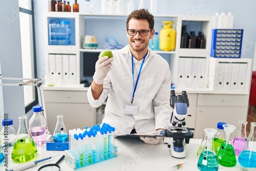 Young hispanic man scientist holding apple at laboratory
