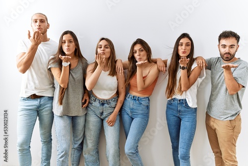 Group of young friends standing together over isolated background looking at the camera blowing a kiss with hand on air being lovely and sexy. love expression.