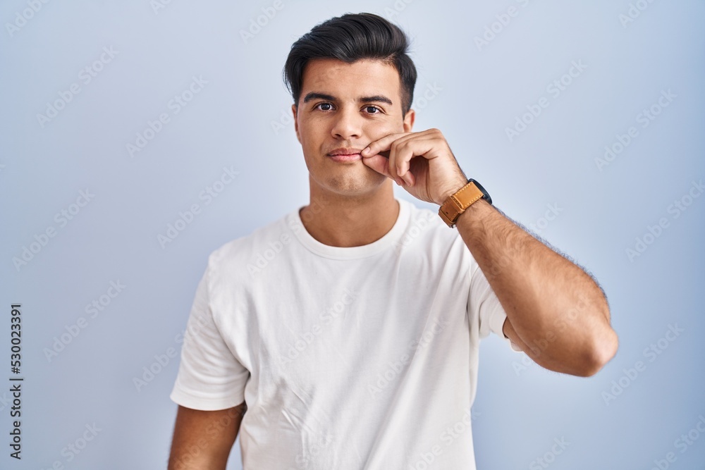 Fototapeta premium Hispanic man standing over blue background mouth and lips shut as zip with fingers. secret and silent, taboo talking