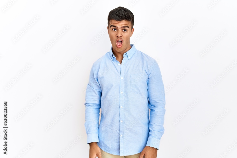 Young hispanic man wearing business shirt standing over isolated background in shock face, looking skeptical and sarcastic, surprised with open mouth Young hispanic man wearing business shirt standing over isolated background in shock face, looking skeptical and sarcastic, surprised with open mouth