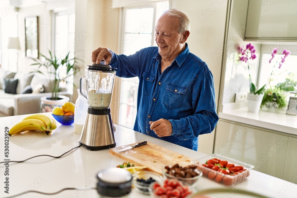 Senior man smiling confident shaking blender at kitchen