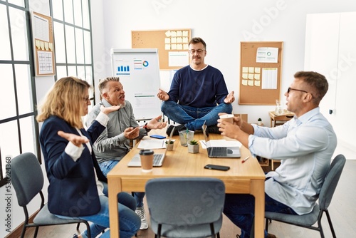Businessman enjoys meditating during meeting. Sitting on desk near arguing partners at the office.