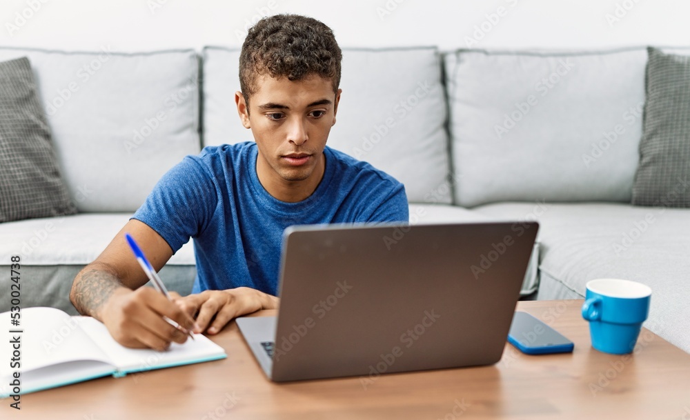 Young hispanic man studying with notebook and laptop at home Young hispanic man studying with notebook and laptop at home