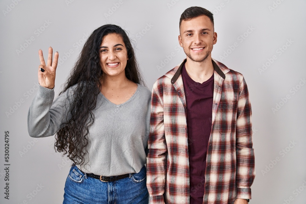 Young hispanic couple standing over white background showing and pointing up with fingers number three while smiling confident and happy. Young hispanic couple standing over white background showing and pointing up with fingers number three while smiling confident and happy.