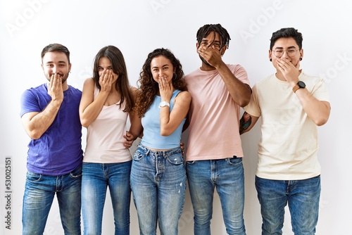 Group of young people standing together over isolated background laughing and embarrassed giggle covering mouth with hands, gossip and scandal concept