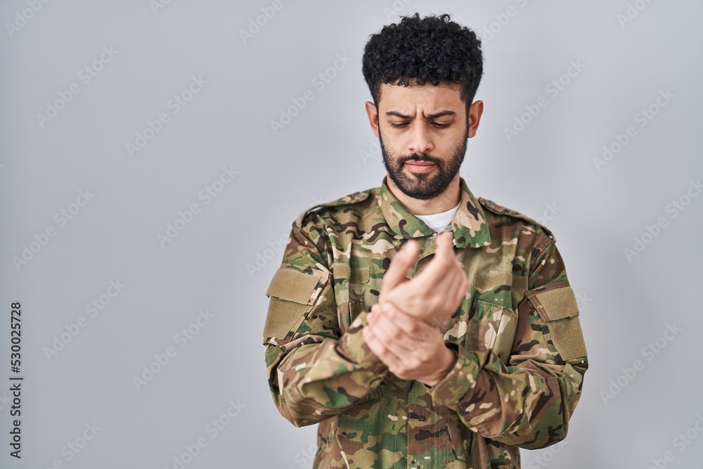 Arab man wearing camouflage army uniform suffering pain on hands and fingers, arthritis inflammation