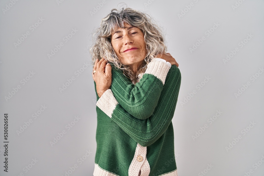 Middle age woman standing over white background hugging oneself happy and positive, smiling confident. self love and self care Middle age woman standing over white background hugging oneself happy and positive, smiling confident. self love and self care