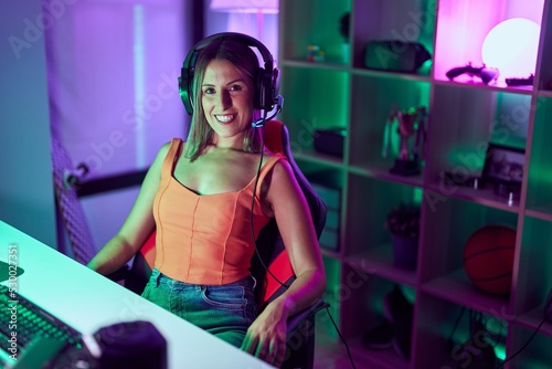 Young beautiful hispanic woman streamer smiling confident sitting on table at gaming room