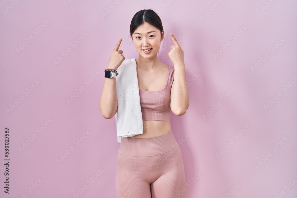 Chinese young woman wearing sportswear and towel smiling pointing to head with both hands finger, great idea or thought, good memory Chinese young woman wearing sportswear and towel smiling pointing to head with both hands finger, great idea or thought, good memory