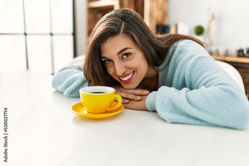 Young woman drinking coffee sitting on table at home Young woman drinking coffee sitting on table at home