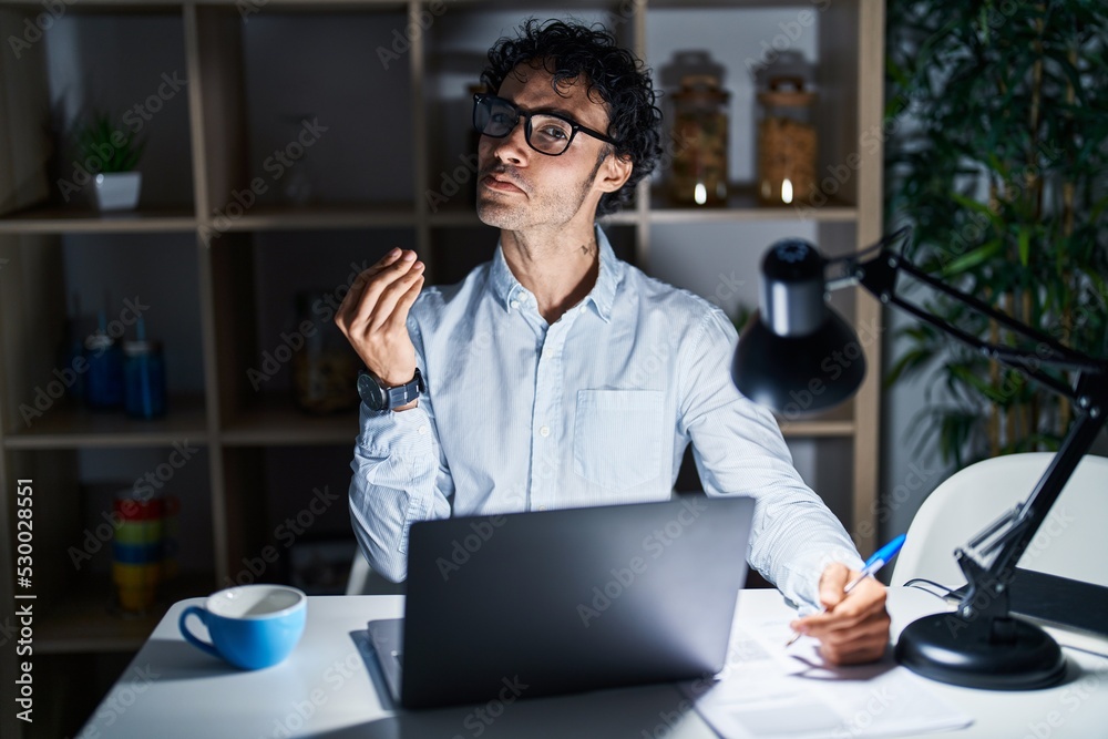 Obraz premium Hispanic man working at the office at night doing money gesture with hands, asking for salary payment, millionaire business