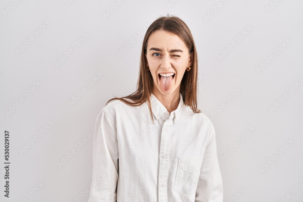 Young caucasian woman standing over isolated background sticking tongue out happy with funny expression. emotion concept.