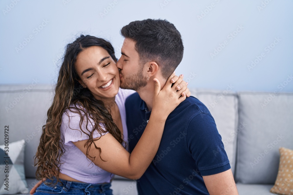Young hispanic couple sitting on sofa hugging each other and kissing at home Young hispanic couple sitting on sofa hugging each other and kissing at home
