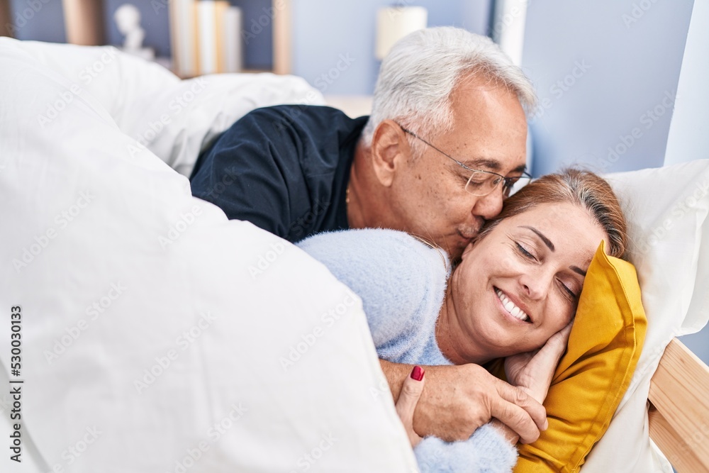 Middle age man and woman couple hugging each other and kissing lying on bed at bedroom Middle age man and woman couple hugging each other and kissing lying on bed at bedroom