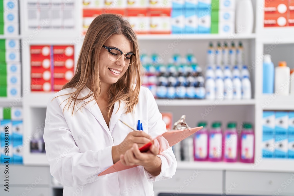Young woman pharmacist writing on document at pharmacy