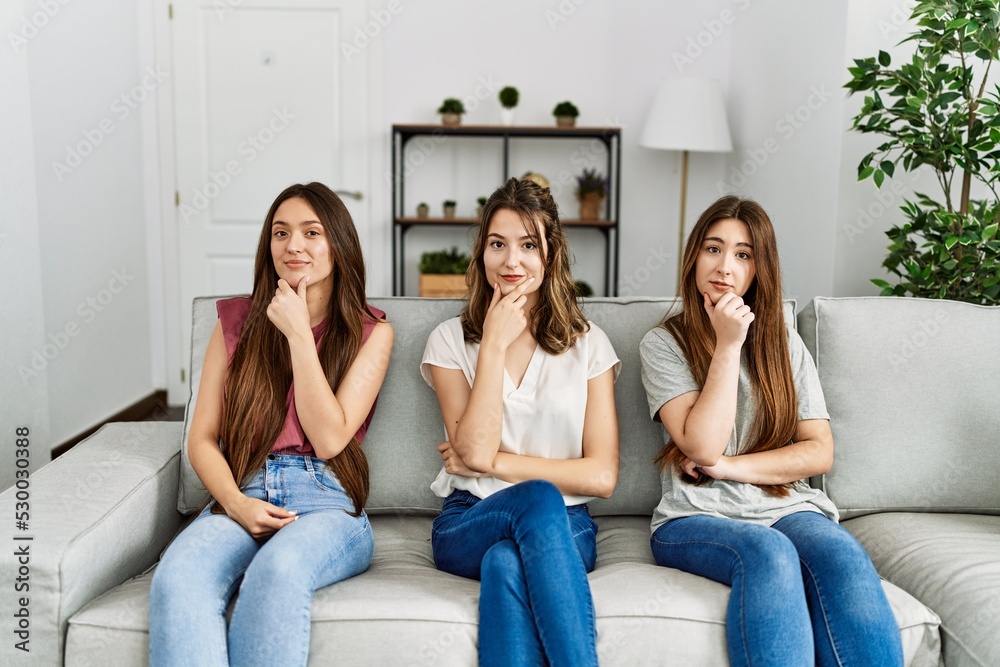 Group of three hispanic girls sitting on the sofa at home looking confident at the camera with smile with crossed arms and hand raised on chin. thinking positive. Group of three hispanic girls sitting on the sofa at home looking confident at the camera with smile with crossed arms and hand raised on chin. thinking positive.
