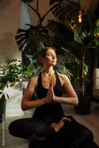 The girl does yoga against the background of green plants in his studio