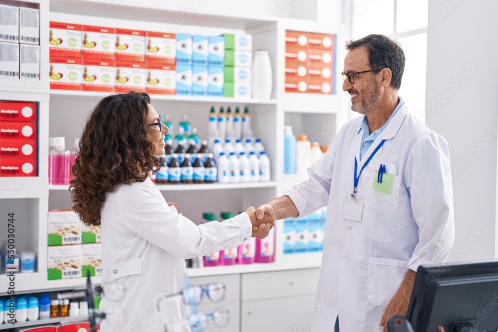 Man and woman pharmacists smiling confident shake hands at pharmacy