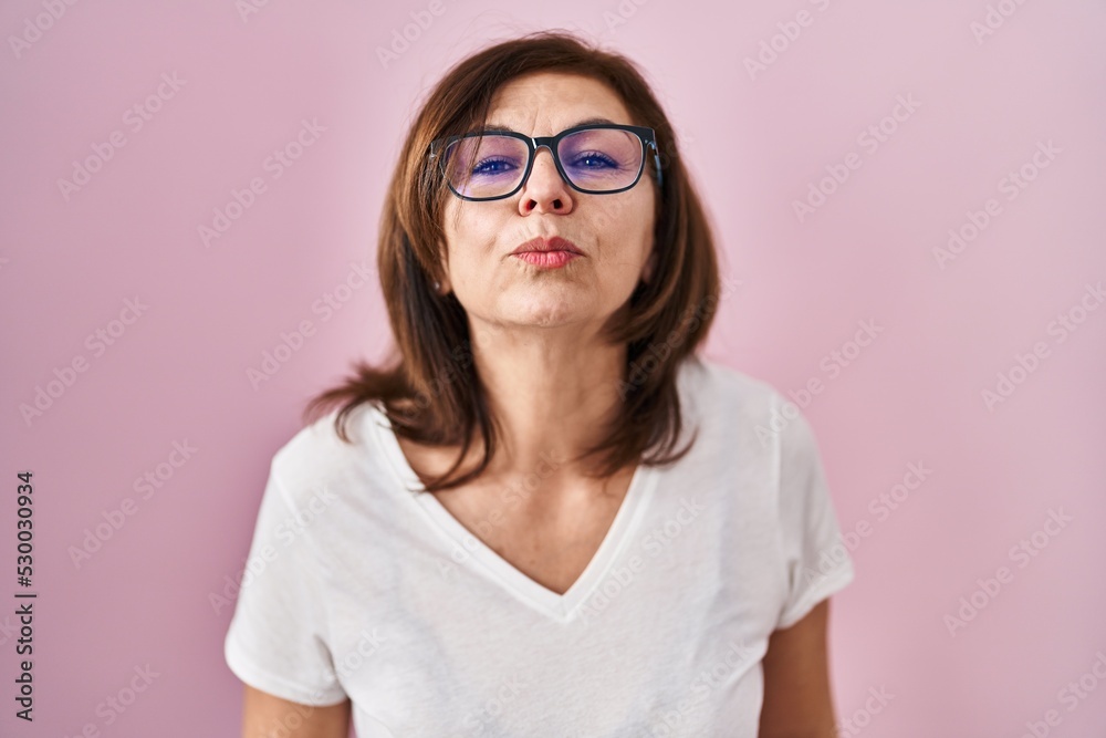 Middle age hispanic woman standing over pink background looking at the camera blowing a kiss on air being lovely and sexy. love expression.