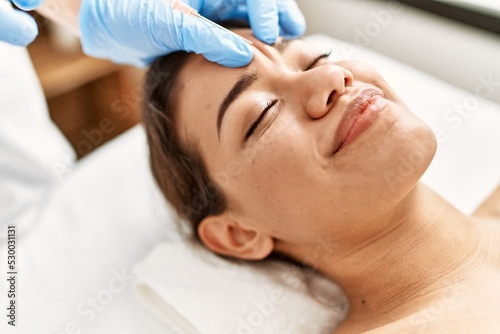 Young latin woman relaxed having anti aging lips treatment at beauty center