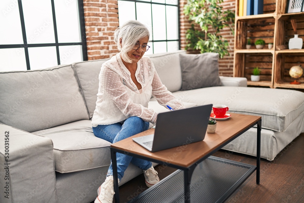 Middle age woman studying using laptop writing on book at home Middle age woman studying using laptop writing on book at home