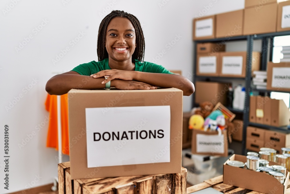 © Krakenimages.com - Young african american woman wearing volunteer uniform leaning on donations package at charity center