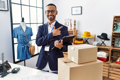 African american man working as manager at retail boutique cheerful with a smile on face pointing with hand and finger up to the side with happy and natural expression