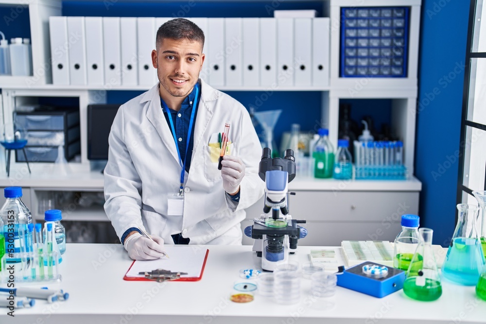 Young hispanic man scientist holding blood test tube at laboratory