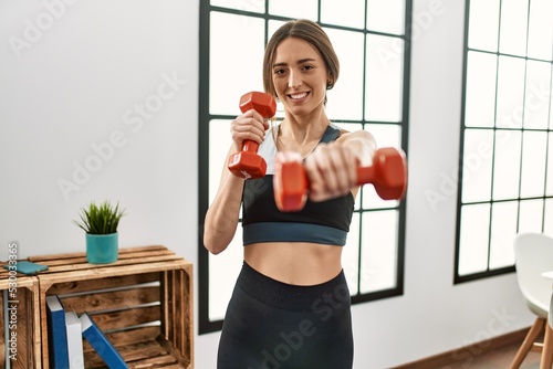 Young hispanic woman smiling confident boxing using dumbbells at home