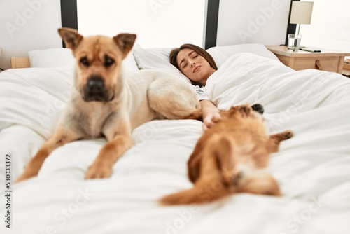 Young hispanic woman sleeping lying on bed with dogs at bedroom © Krakenimages.com