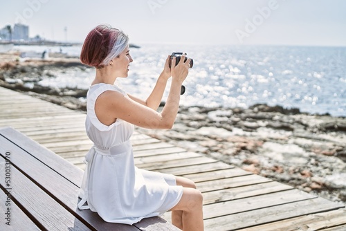 Young caucasian girl using professional camera sitting on the bench at the beach.