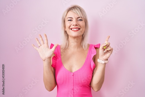 Young caucasian woman standing over pink background showing and pointing up with fingers number six while smiling confident and happy.