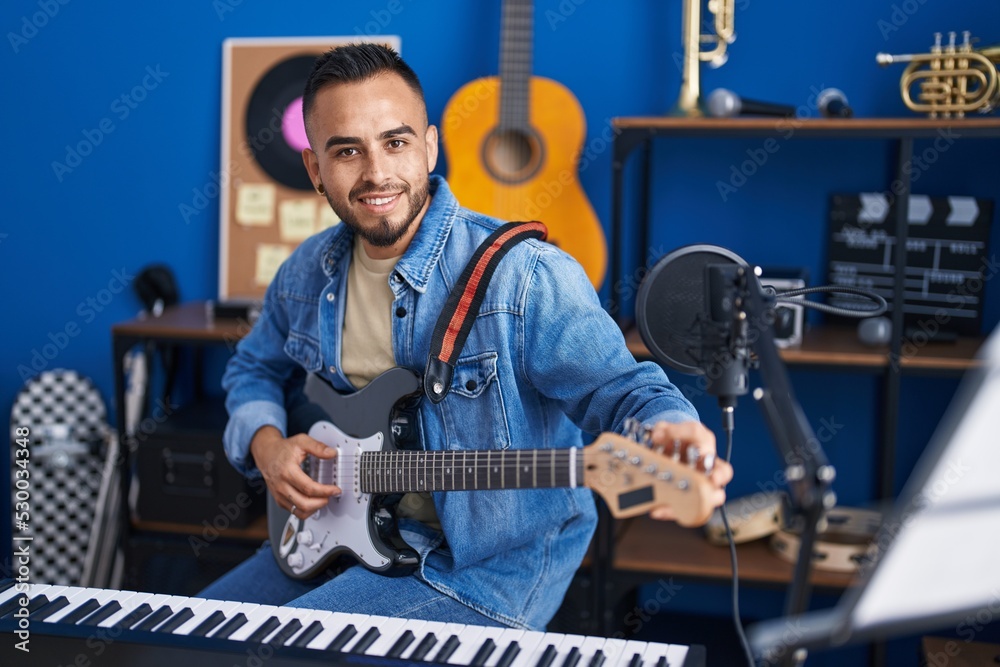 Fototapeta premium Young hispanic man musician smiling confident playing electrical guitar at music studio