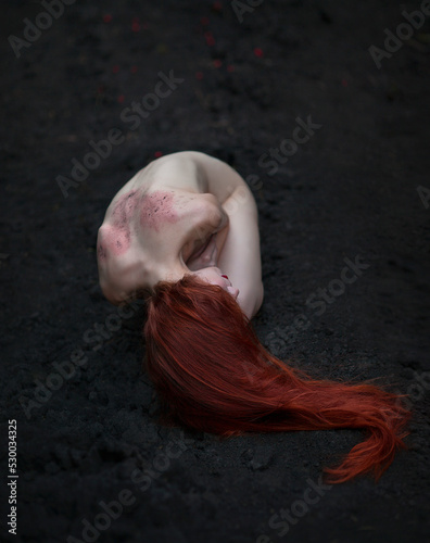 A naked red-haired woman in a creepy pose is lying on the ground. No face visible. The concept of horror.