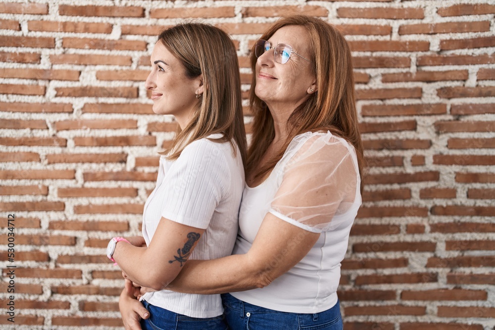 Hispanic mother and daughter wearing casual white t shirt looking to side, relax profile pose with natural face and confident smile.