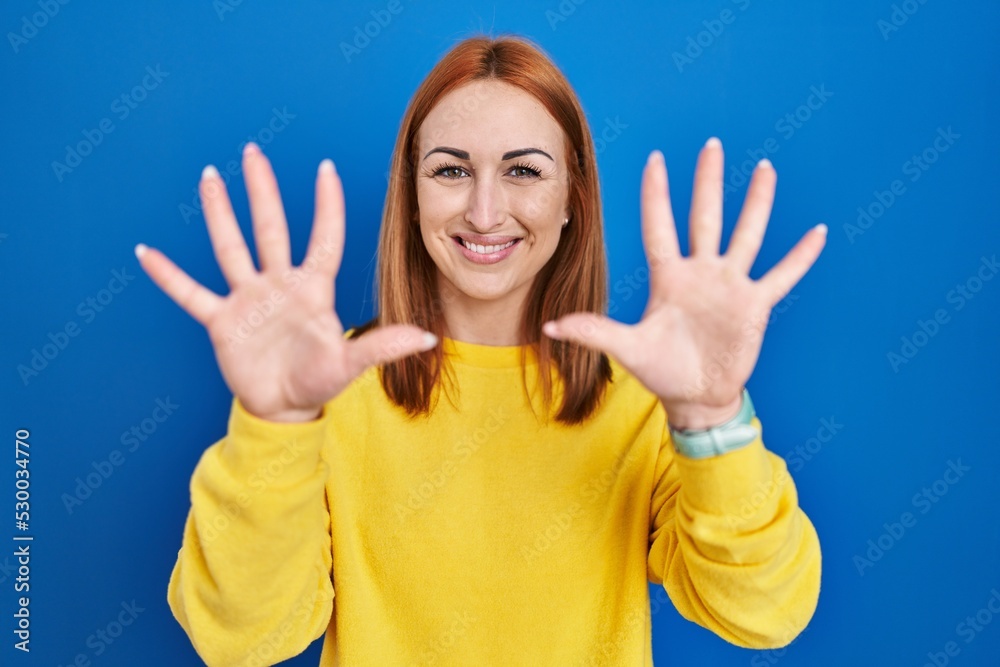 Young woman standing over blue background showing and pointing up with fingers number ten while smiling confident and happy.