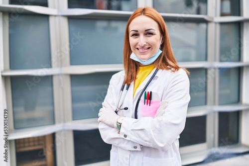 Young caucasian woman doctor wearing medical mask standing with arms crossed gesture at hospital